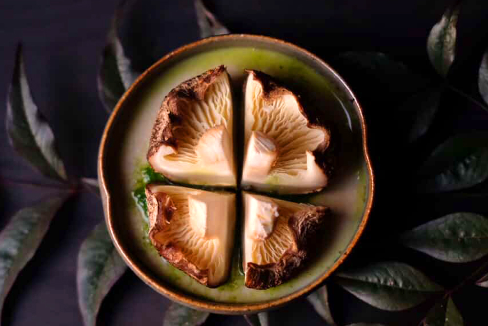 二品目は‟原木椎茸のフラン“。椎茸の軸から取った出汁をベースに仕立てた茶碗蒸しに、大根の葉とナスタチウムで作るソースを流し、竹の葉に包んで炭火焼きにした椎茸を盛り付けている。焼成の途中で竹の葉を開き、蕎麦焼酎を霧吹きで吹きかけながらじっくり火を入れることで香ばしさを引き出し、椎茸の濃厚な味わいが際立つ一品に仕上げてある