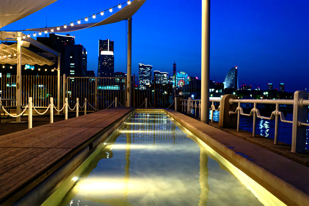 横浜港を眺めながら入浴できる足湯。夏は足水としても活用するという。日中は無料、17時以降は300円で入浴することができ、カフェカウンターで整理券を貰うシステムになっている。開業以来非常に人気が高く、既に行列もできている。日中も楽しいが、横浜港の夜景を見ながら入る足湯もまた、一興だ