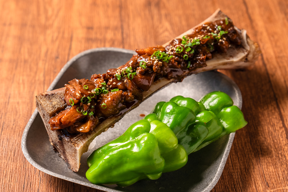 パリパリピーマンでドテ煮を食べる‟渋谷のパリピ”。なんと！トロトロになるまで脊髄を煮込んだ牛骨を縦割りにし、その上にドテ煮がかかっているダイナミックな一皿。その美味しさを、ネーミングの面白さと共に味わってもらいたい